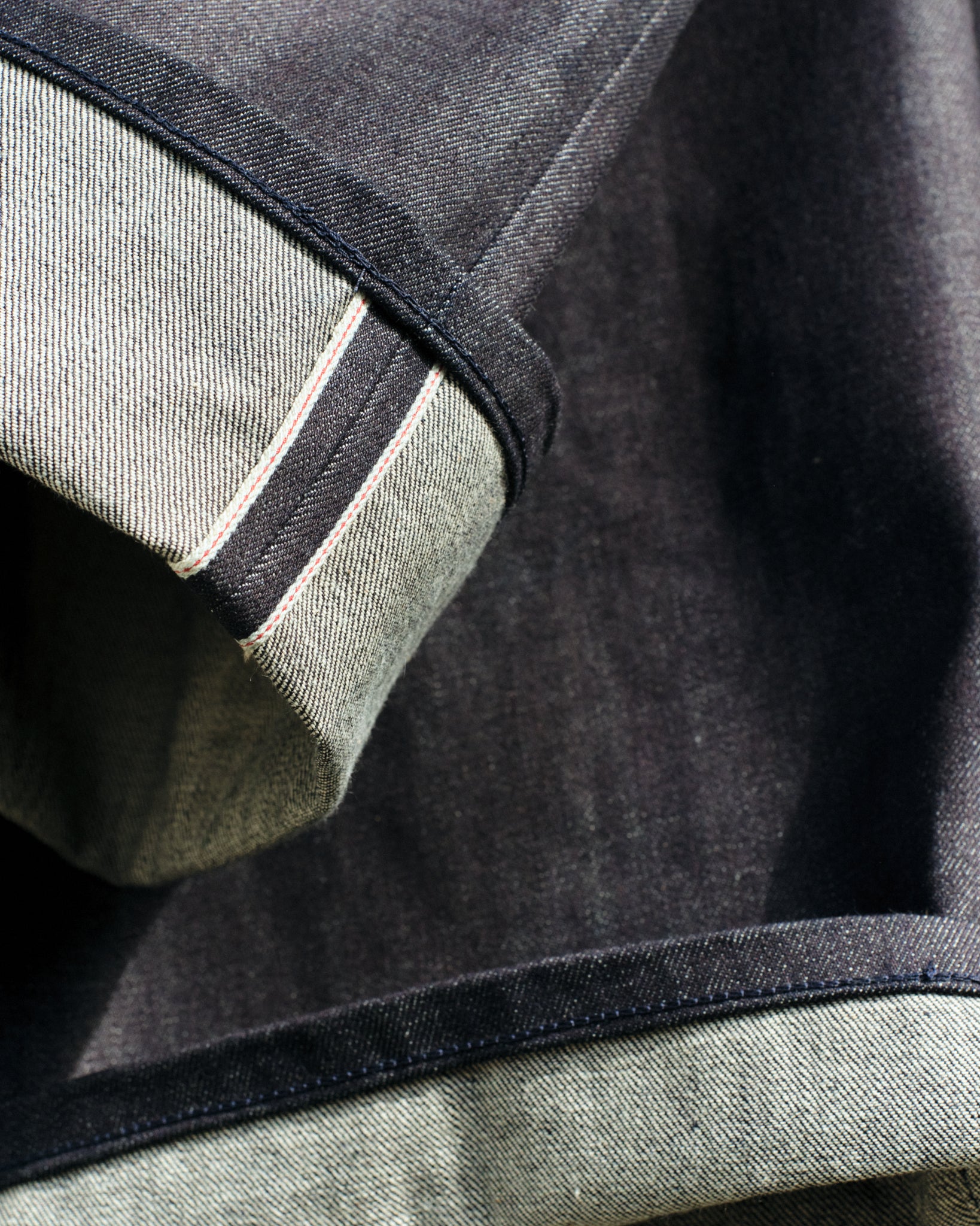 Close up of folded hems of a pair of japanese selvedge denim, showing a white/red selvedge and clean tonal chainstitch hem seam. Made to order and limited edition by Marloes Editions