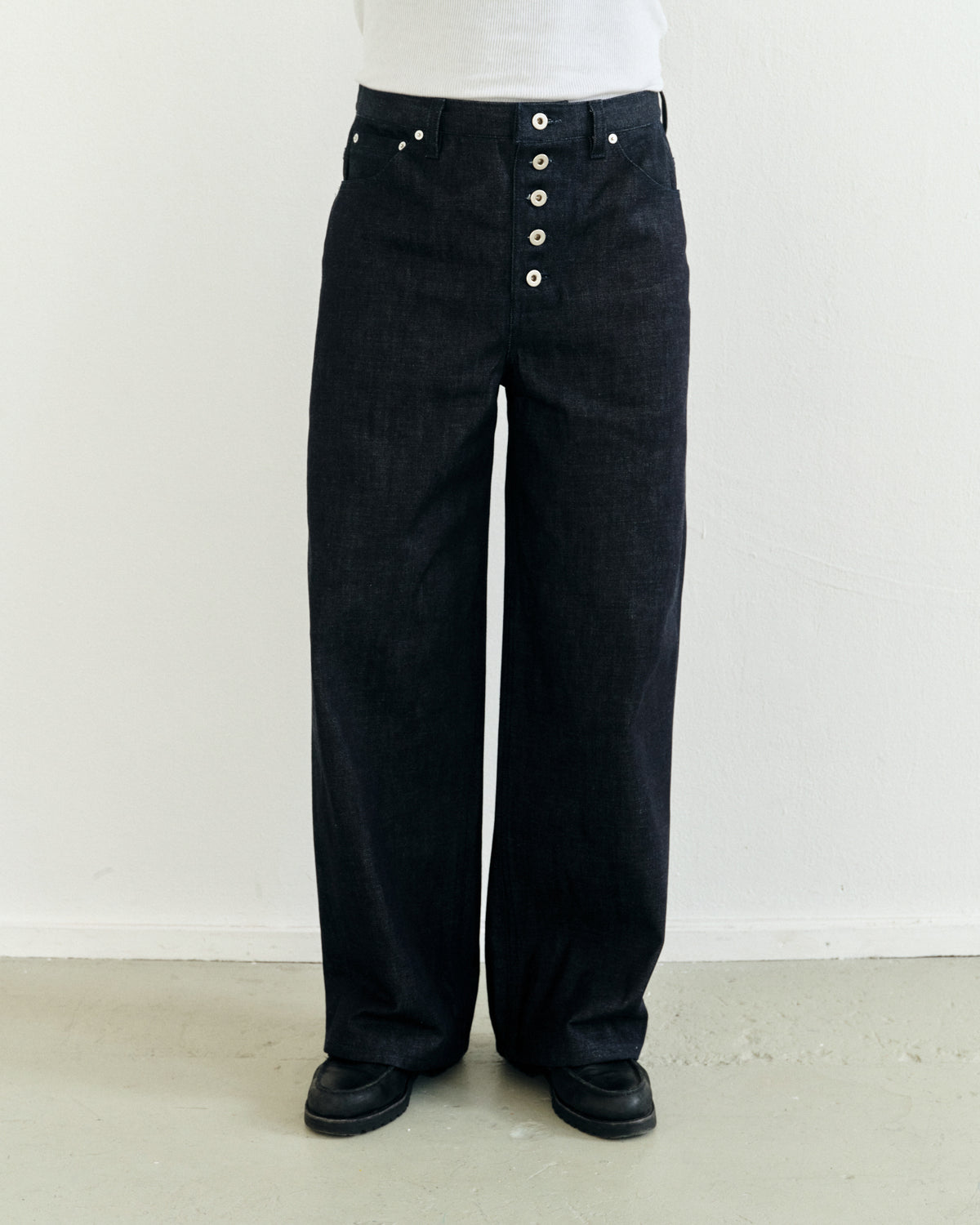 Dark japanese selvedge denim pants with exposed button details worn by a person against a white background