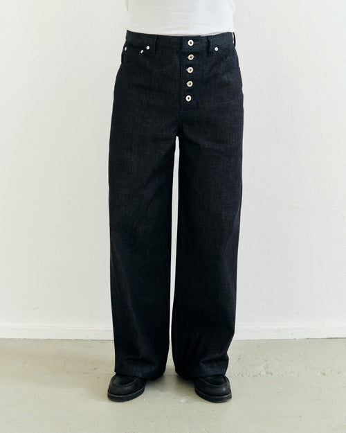 Dark japanese selvedge denim pants with exposed button details worn by a person against a white background