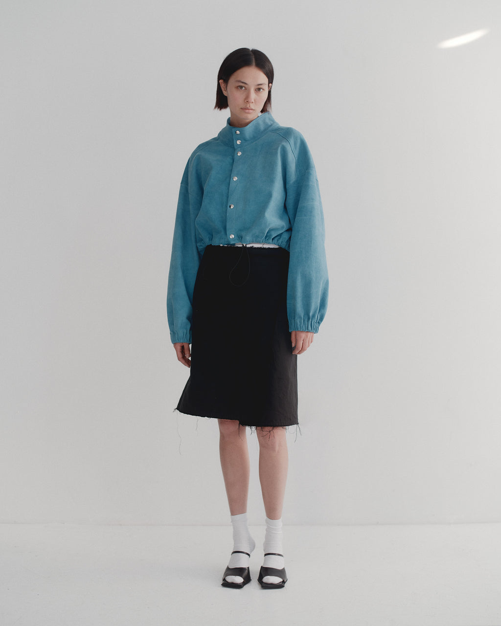 Person wearing a bright blue brushed cotton studio bomber and black skirt on a white background