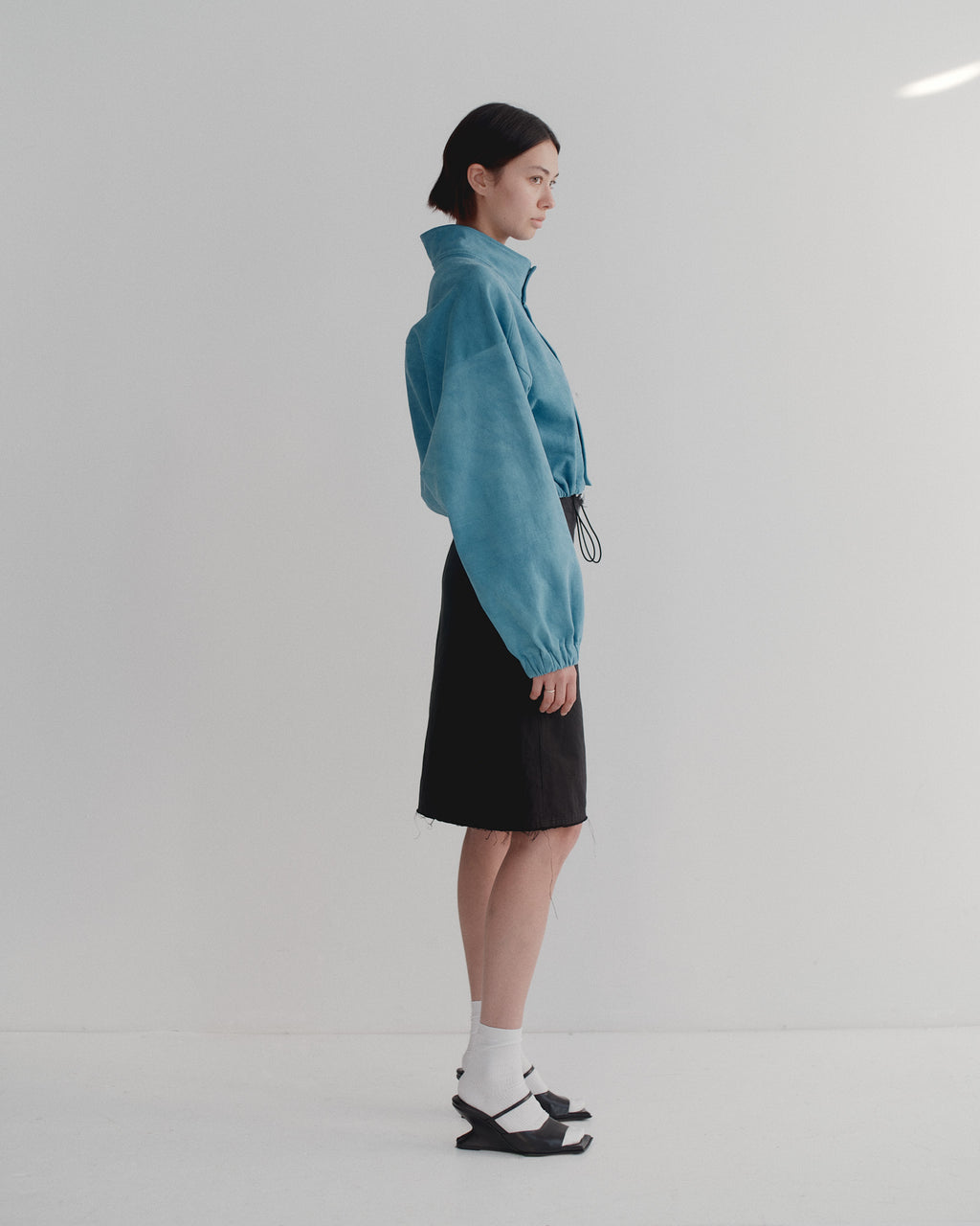 Model wearing a bright blue brushed cotton studio bomber jacket with high collar and black skirt on a white background