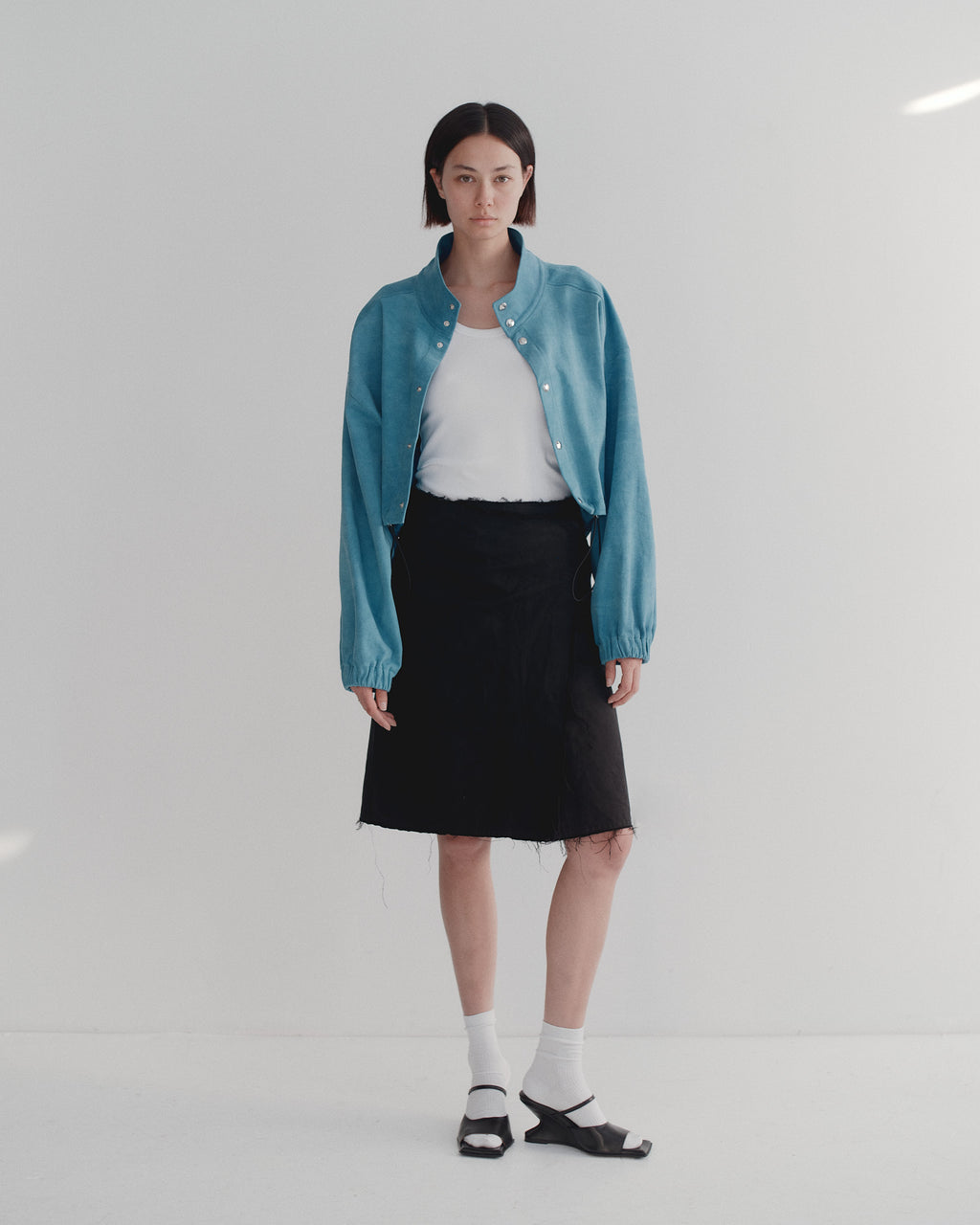 Model wearing a bright blue brushed cotton bomber  jacket, white tanktop, black skirt, and white socks in heels on a white background