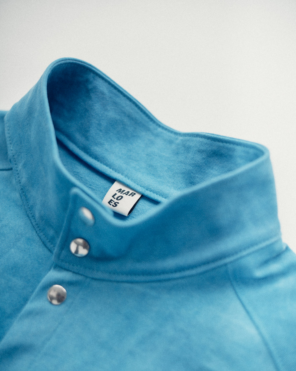 Close-up of the Studio Bomber collar with buttons and a label of Marloes Editions on a light gray background