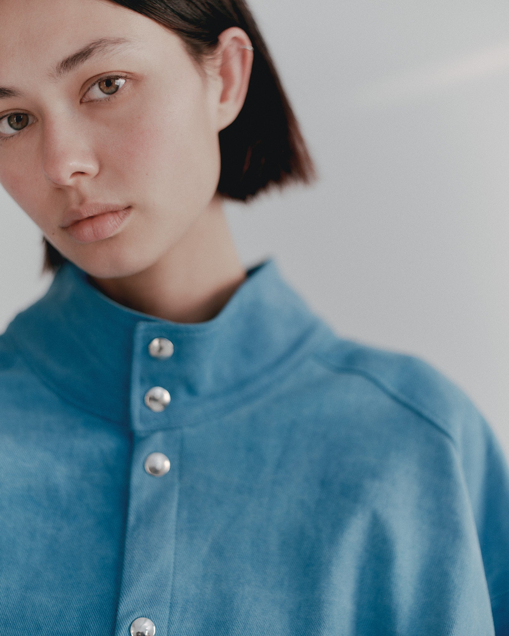 Model wearing the bright blue Studio Bomber with a high collar and silver snap buttons. Fabric showing hand dyed qualities and a deadstock Burberry brushed cotton premium effect. Limited Edition Made to order by Marloes Editions