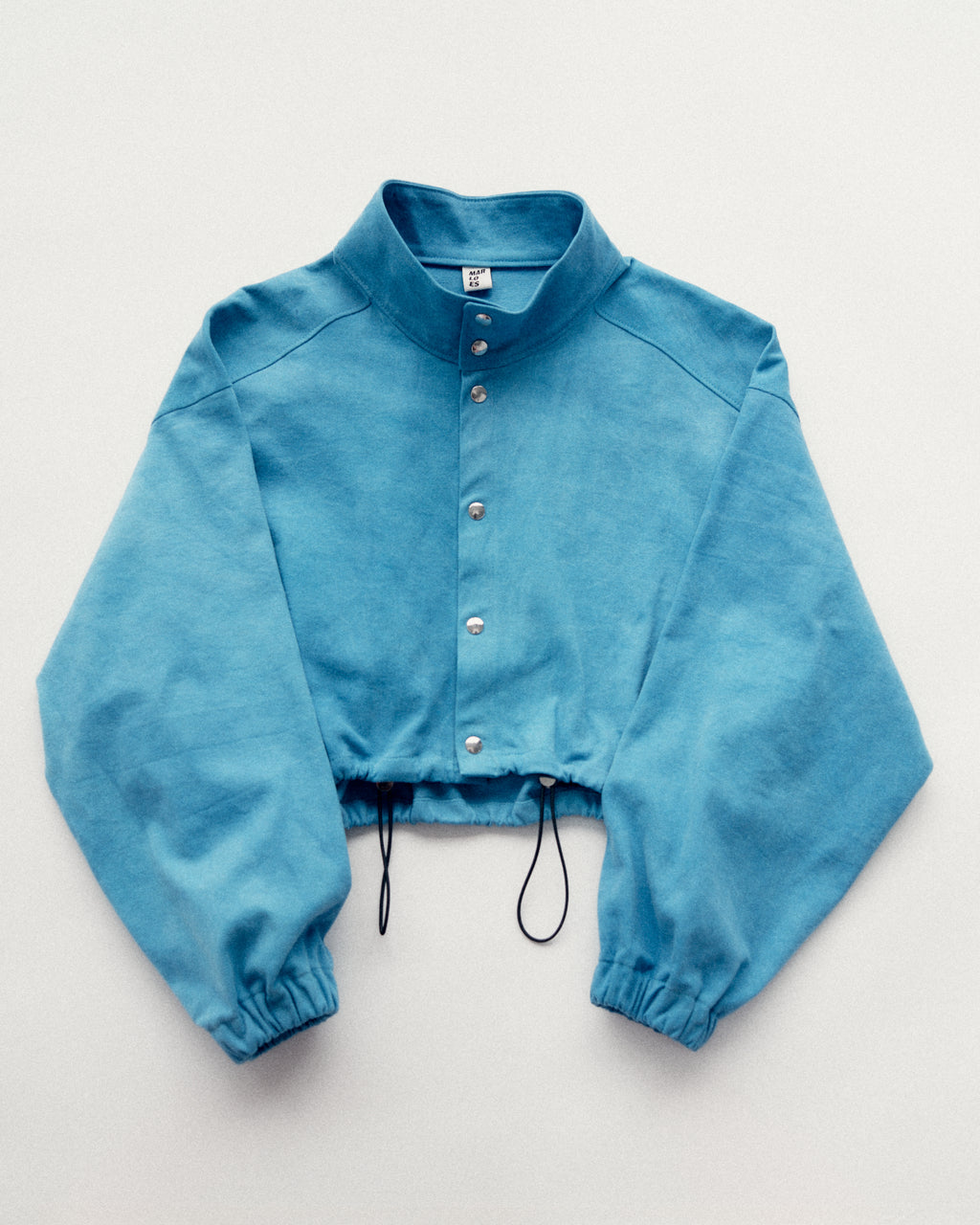 Bright blue hand dyed Studio Bomber made to order by Marloes Editions showing silver snap buttons and an adjustable elastic hem 