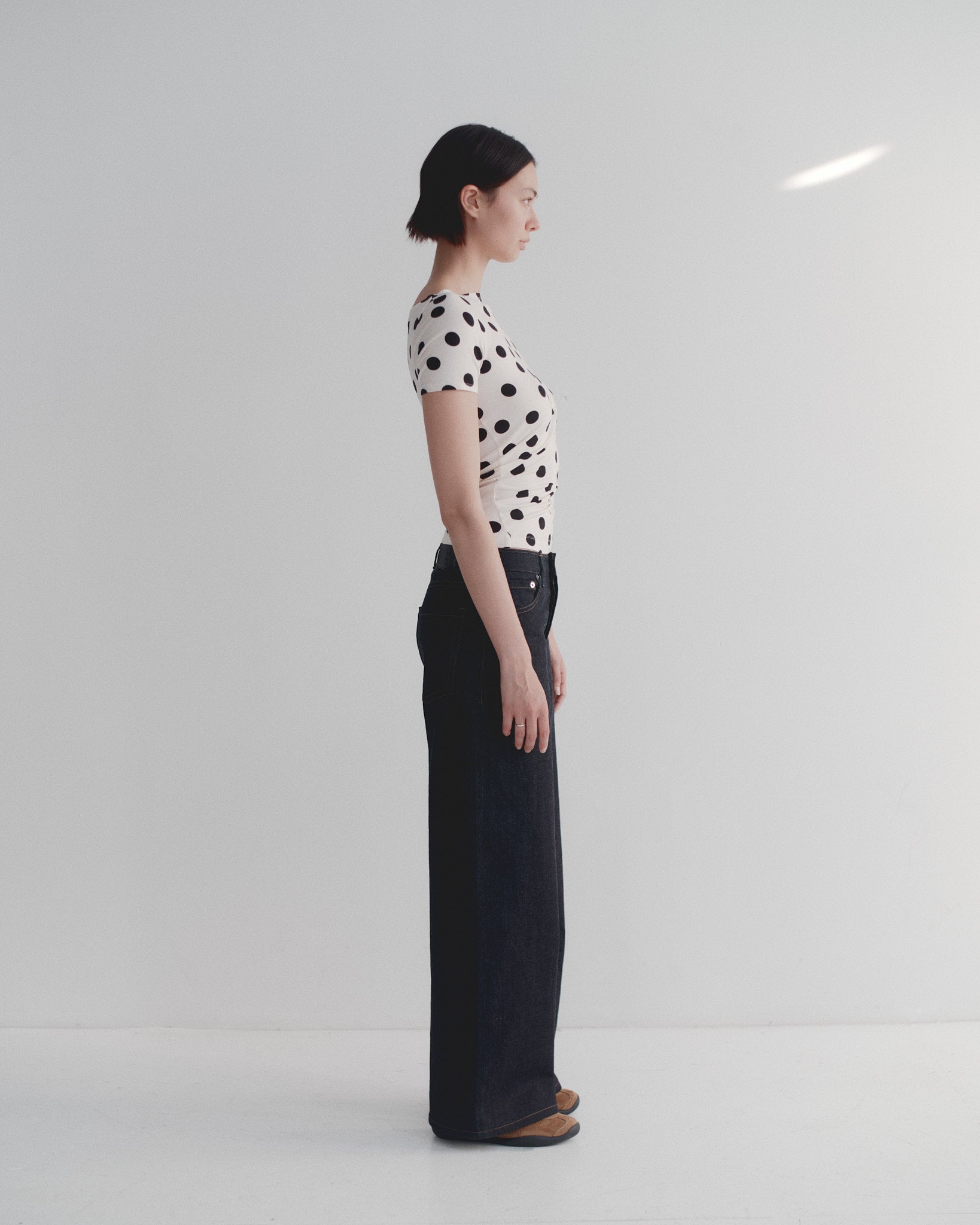Person wearing a polka dot shirt and dark japanese selvedge denim pants standing against a white background